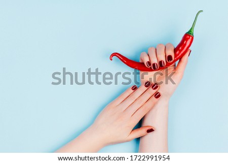 Classic red manicure with chili pepper on pastel blue background. Skin care concept. Flat lay style.