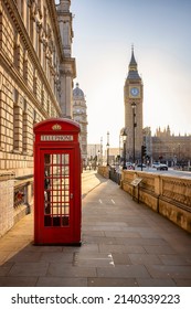 A classic, red telephone booth in front of the Big Ben clocktower in London, Westminster, during golden sunrise without people