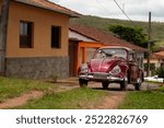 classic red vintage car, parked on a street, in front of houses, mountainous landscape in the background