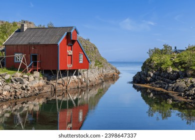 A classic red wooden house on the shores of the Lofoten Islands, Norway, gleaming in the summer sunshine against a backdrop of a bright blue sky - Powered by Shutterstock