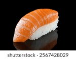 Classic salmon nigiri sushi featuring a fresh slice of raw salmon placed on seasoned sushi rice, displayed on a reflective black background.