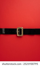 A classic Santa Claus belt with a gold buckle lying on a bright vertical red background, symbolizing Christmas and holiday cheer