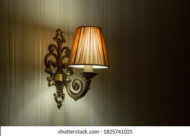 Classic sconce with turned on bulb under lampshade hanging on wall.