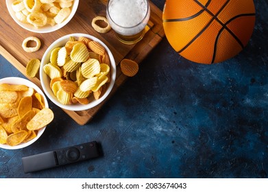 A Classic Set Of Sports Fans - A Glass Of Beer, Potato Chips, Onion Rings On A Wooden Tray. Nearby On The Table Is A Television Remote Control And A Basketball. Watching Sports Matches On TV.