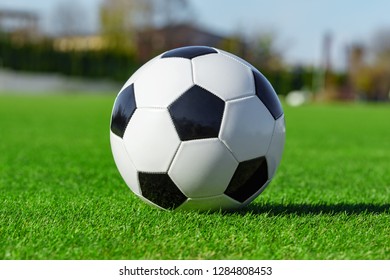 Classic Soccer Ball Lying On The Bright Green Grass On The Football Field In The Background Of The Stands For The Fans At The Sports Stadium Close-up In A Large Sports Center For Football Players