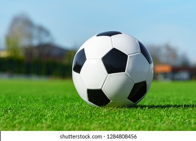 Classic Soccer Ball Lying On The Bright Green Grass On The Football Field In The Background Of The Stands For The Fans At The Sports Stadium Close-up In A Large Sports Center For Football Players