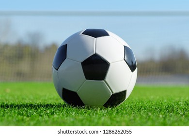 Classic Soccer Ball Lying On The Bright Green Grass On The Football Field In The Background Of The Stands For The Fans At The Sports Stadium Close-up In A Large Sports Center For Football Players