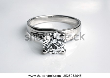 a classic solitaire ring with a large, round-cut diamond set in a prong setting. The diamond is clear and sparkling, mounted on a sleek, reflective silver-toned metal band.