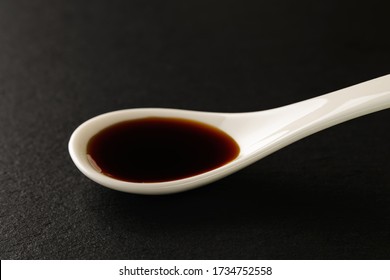 Classic Soy Sauce In A White Chinese Porcelain Spoon On A Black Stone Serving Board. Sauces And Seasonings For Meat, Fish And Vegetables. Front View.