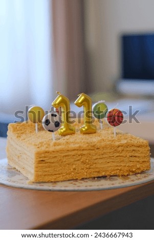 The classic square Napoleon cake is decorated with eleven candles and sports balls - football, basketball, volleyball, tennis. Birthday confectionery. Festive bakery. Bright celebration at home. 