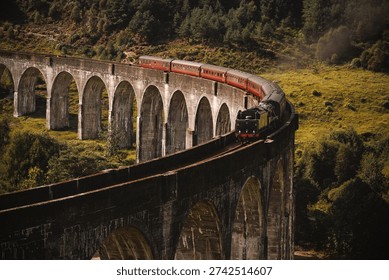 A classic steam engine pulls red carriages across the arched concrete Glenfinnan Viaduct surrounded by lush green hills.