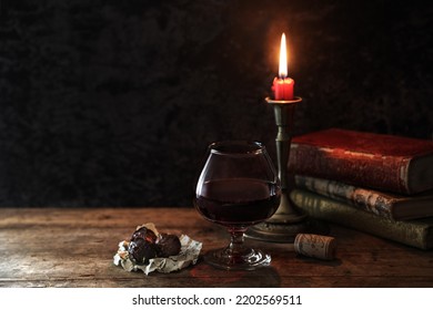 Classic still life with vintage books and candle with a glass of red wine and chocolates at rustic dark background - dark and moody - Shutterstock ID 2202569511