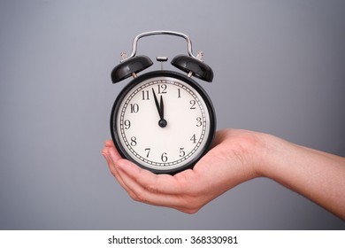 Classic Style Alarm Clock In Woman Hand Against Grey Background. Three Minutes Before Deadline.