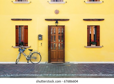 Classic style house entrance (yellow walls, wooden door and windows decorates with flowerpots) and lonely bicycle - Powered by Shutterstock