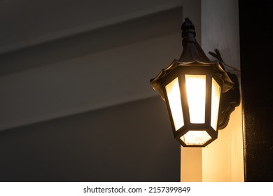 A Classic Style Street Lighting Lamp Is Glowing In Orange Warm Light Shade In Evening Night Time With Background Of Building Structure. Photo Contained Noise Due To Dark Condition. Selective Focus.