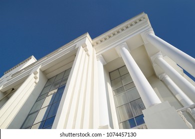 Classic style white building facade detail with pillars against clear blue sky. Modern architecture. Low angle view