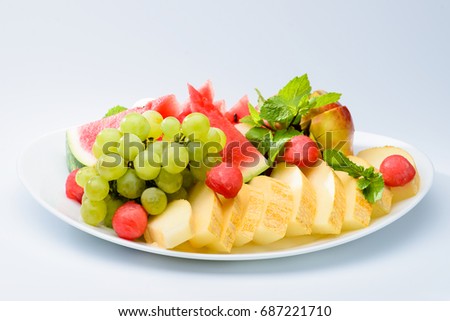 classic summer Italian food. Beautifully decorated fruit platter with watermelon, melon, apricot and grapes on a white plate, light background