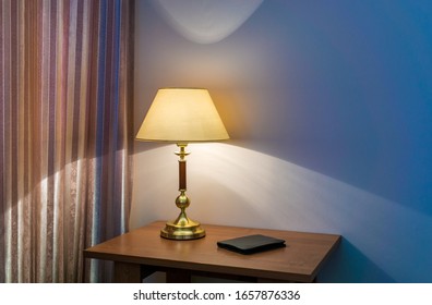 Classic table lamp with turned on bulb under lampshade is against wall with blue wallpaper. Copy space