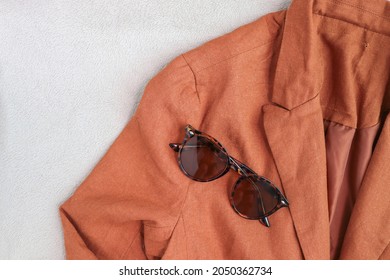 Classic textured turtle sunglasses on an earthy, brown blazer on a light gray background - autumn fashion concept.