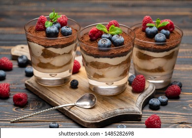 Classic tiramisu dessert with blueberries and strawberries in a glass cup on cutting board on wooden background
