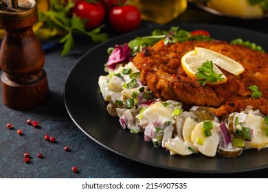 Classic, traditional Viennese sirloin schnitzel. Served on potato salad. Breaded. Dark background.