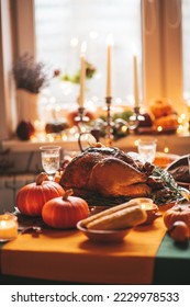 Classic USA Thanksgiving day dinner with holiday autumn decor and candles. Family dining room table set with delicious golden roasted turkey on platter garnished rosemary and fresh small pumpkins