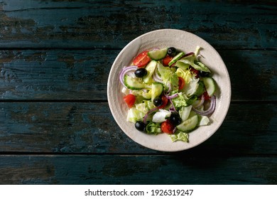 Classic vegetable salad with tomatoes, cucumber, onion, salad leaves and black olives in white ceramic plate. Dark wooden background. Flat lay, copy space