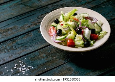 Classic vegetable salad with tomatoes, cucumber, onion, salad leaves and black olives in white ceramic plate. Dark wooden table.