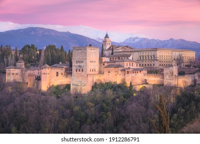 Classic view with pink sunset or sunrise sky of Charles V Palace, the iconic Alhambra and Sierra Nevada Mountains from Mirador de San Nicolas in the albaicin old town of Granada, Andalusia, Spain.