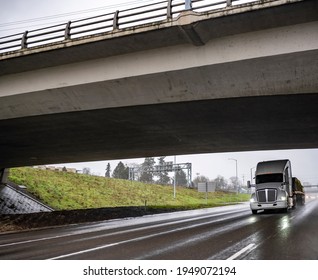 Classic White Long Haul Big Rig Bonnet Semi Truck Tractor Transporting Fixed With Slings Heavy Commercial Cargo On Flat Bed Semi Trailer Running On The Wet Highway Road At Rain Weather Condition