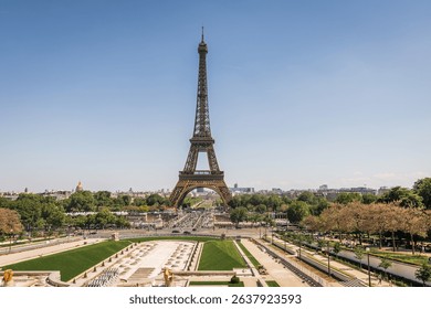 A classic wide-angle view of the Eiffel Tower in Paris, standing tall against a clear blue sky,