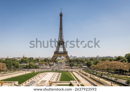 A classic wide-angle view of the Eiffel Tower in Paris, standing tall against a clear blue sky,