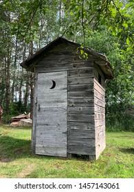 A Classic Wooden Outhouse With A Crescent Moon Cutout In The Door. 