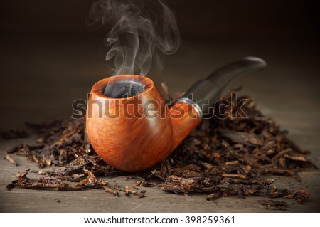 Classic wooden pipe with smoke and tobacco pile on vintage wood.