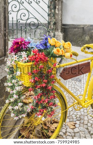 Classic Yellow bicycle, with colorful flowers into a straw basket , parked in a street