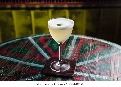 A classic yellow sour cocktail with foam in a nick and nora glass with lime zest garnish