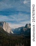 Classic Yosemite Valley vista with El Capitan and Half Dome in moody afternoon light. Dramatic viewpoint captures iconic tunnel view of famous national park.