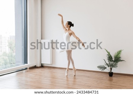 Classical Ballet dancer side view. Beautiful graceful ballerina practice ballet positions in white tutu skirt near large window in white light hall. Ballet class training, high-key soft toning.