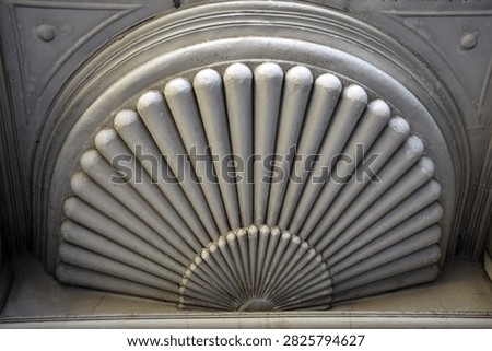 Classical decorative architectural element featuring a fan-shaped sunburst or seashell relief carved in light stone or plaster. Elegantly detailed Art Deco or Art Nouveau motif on an urban building facade, capturing timeless geometric craftsmanship and light and shadow dynamics.
