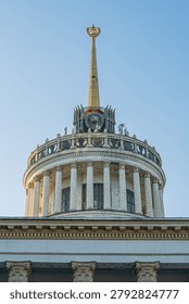 Classical governmental building featuring circular base, fluted columns, domed roof adorned with emblem and decorative motifs, contrasting metallic spire capped with golden star symbolizing historic.