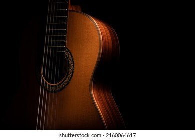 Classical guitar close up, dramatically lit on a black background with copy space.  