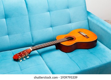 Classical Guitar Laying On A Blue Sofa, Left Behind, Nobody Around, Closeup. Practicing A Musical Instrument, Learning To Play Guitar, Staying At Home Activities, Abstract Music Concept, No People