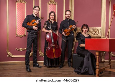 Classical Music Quartet Posing After The Concert With Their Instruments In Hall And Looking At Camera. Studio Shot.