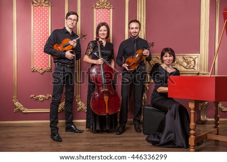 Classical music quartet posing after the concert with their instruments in hall and looking at camera. Studio shot.