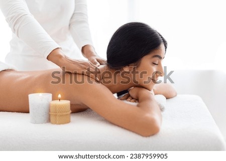 Classical neck and back massage, closeup, side view. Young indian woman enjoying spa treatment at salon. Wellness, beauty and health care concept