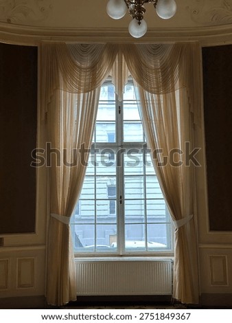 Classical palace room window with elegant draped curtains, decorative ceiling light fixture and ornate wall molding in period interior