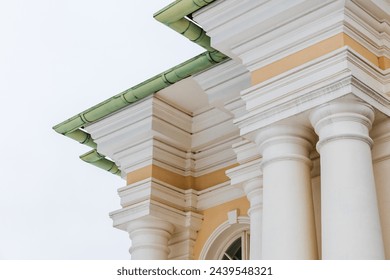 Classical portico with yellow and white details under green roof. Pillars and corners