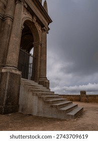 Classical stone columns and weathered steps frame the entrance to the historic Santuari Sant Salvador monastery on Mallorca, showcasing traditional Mediterranean religious architecture under dramatic cloudy skies.