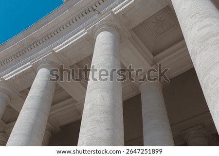 Classical white marble columns with ornate capitals and decorative moldings viewed from below against blue sky