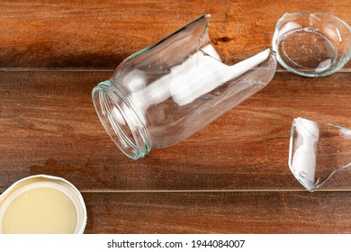 A classical wide mouth twist open glass jar has dropped and shattered into pieces. The sharp edges are exposed and pose danger.  Kitchen accident concept with empty glass jar broken into pieces.